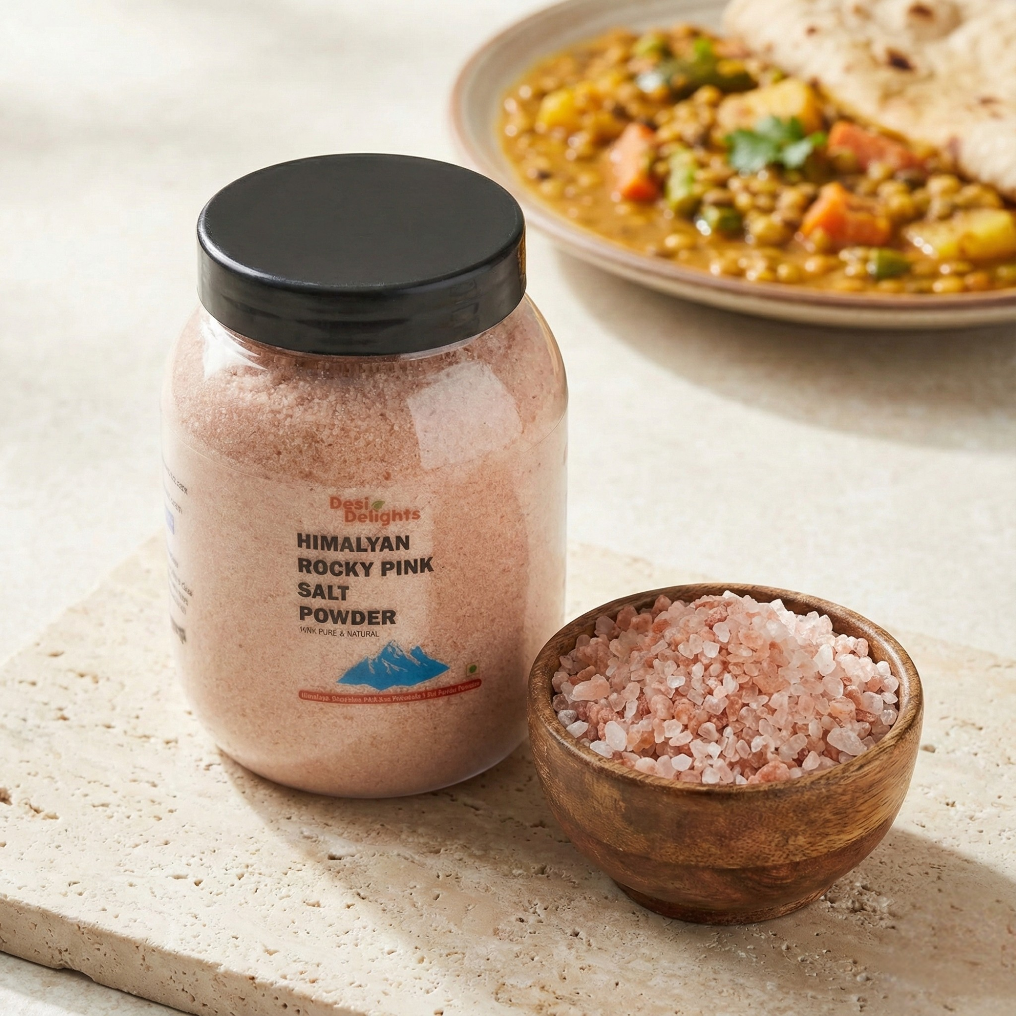 Jar of Himalayan Rocky Pink Salt Powder with a bowl of salt and a plate of curry in the background.