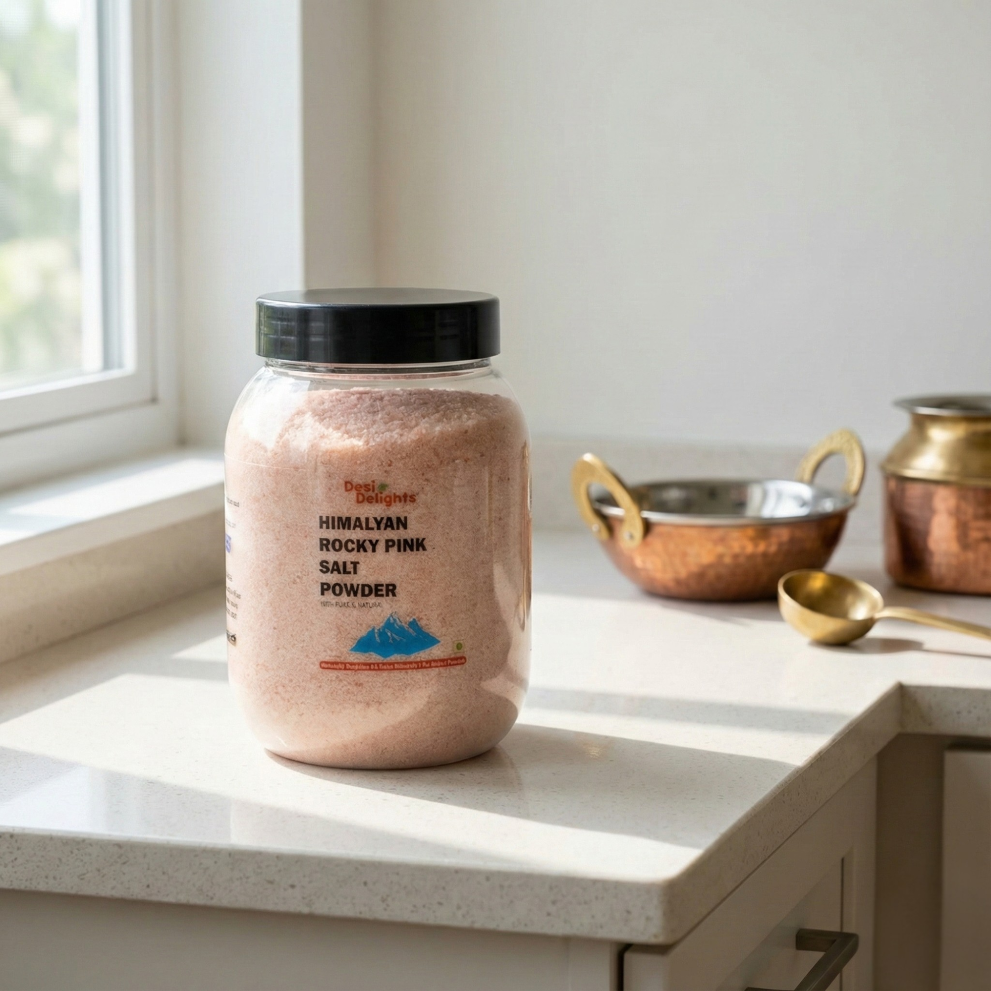 Jar of Himalayan Rocky Pink Salt Powder on a kitchen counter with copper pots and a spoon.